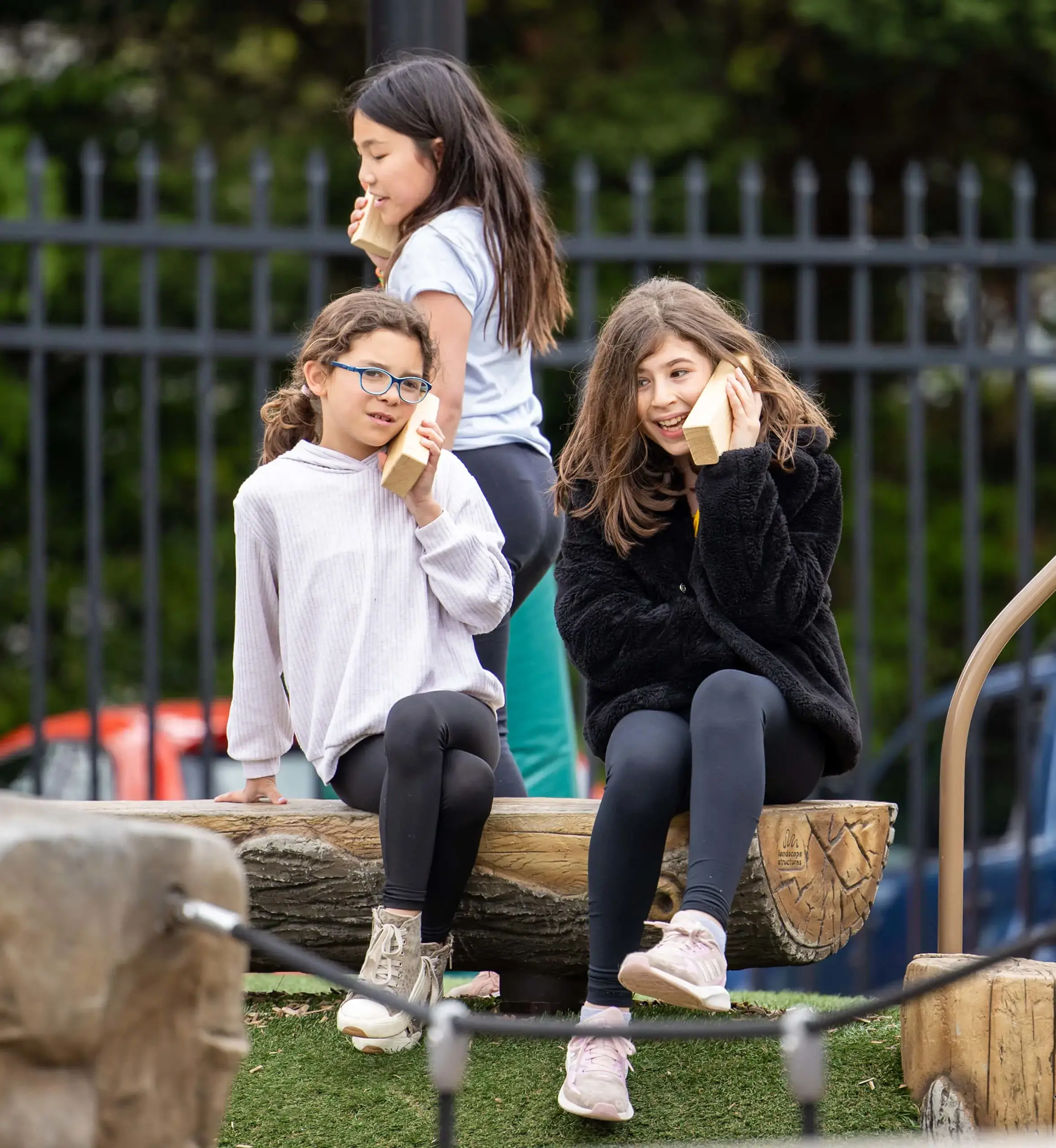 Three girls pretending to use wood blocks as phones