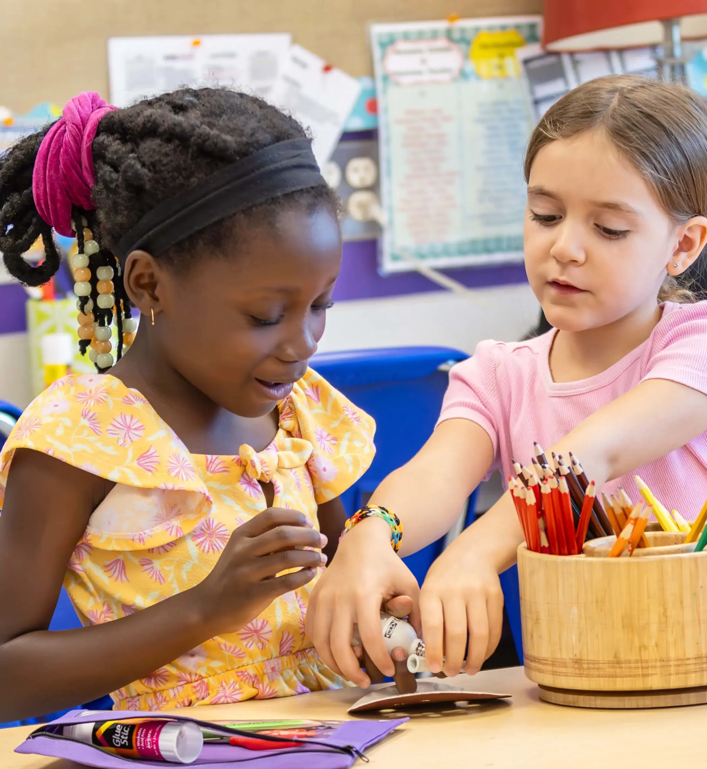 two little girls at a desk with colored pencils