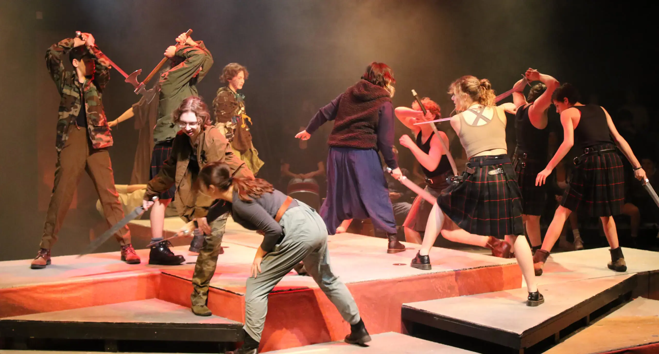 students engaged in a fake sword fight on stage