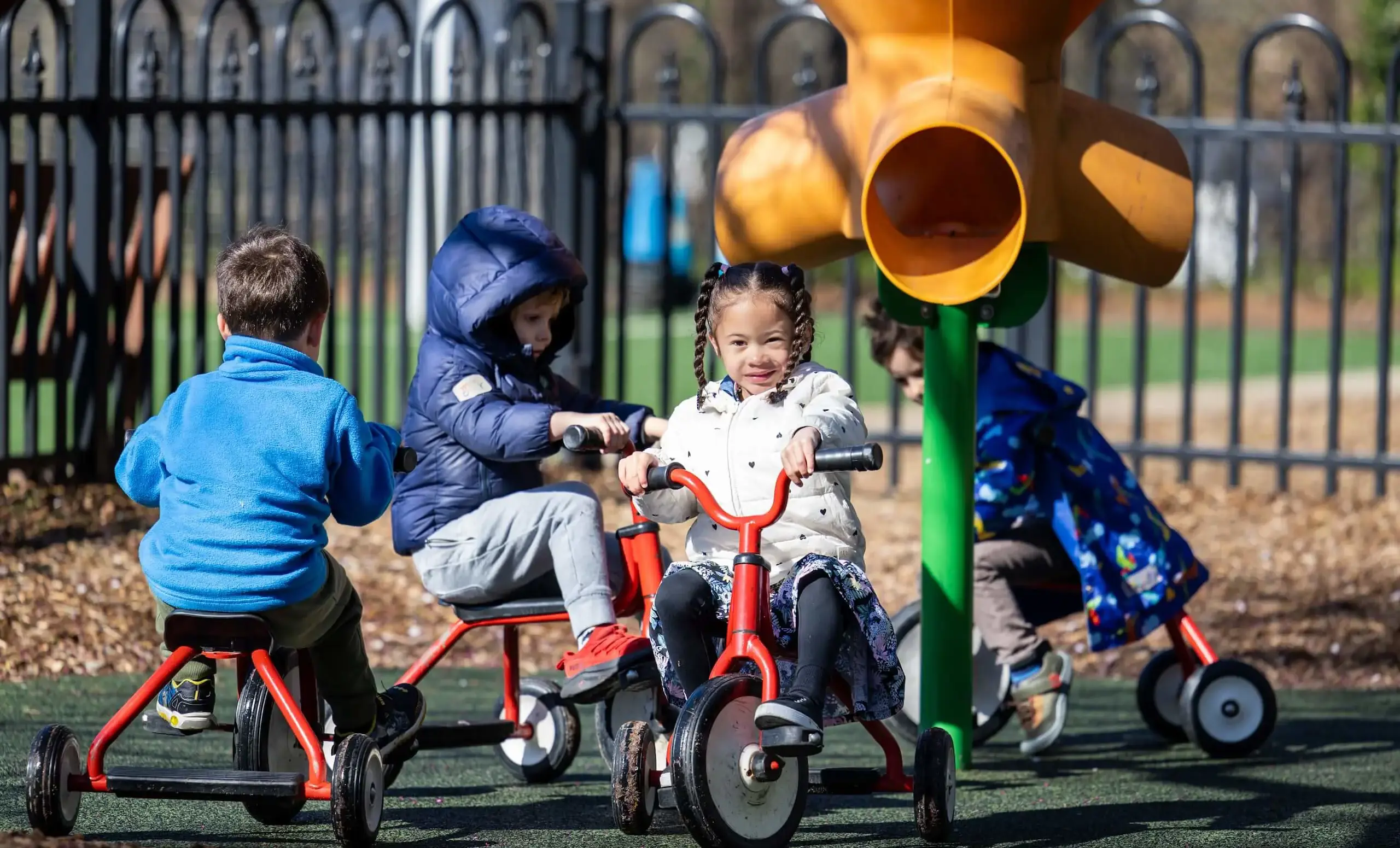 four children riding tricycles on a playground